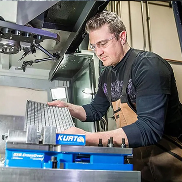 Machinist wearing safety glasses positions a metal workpiece in a milling machine.