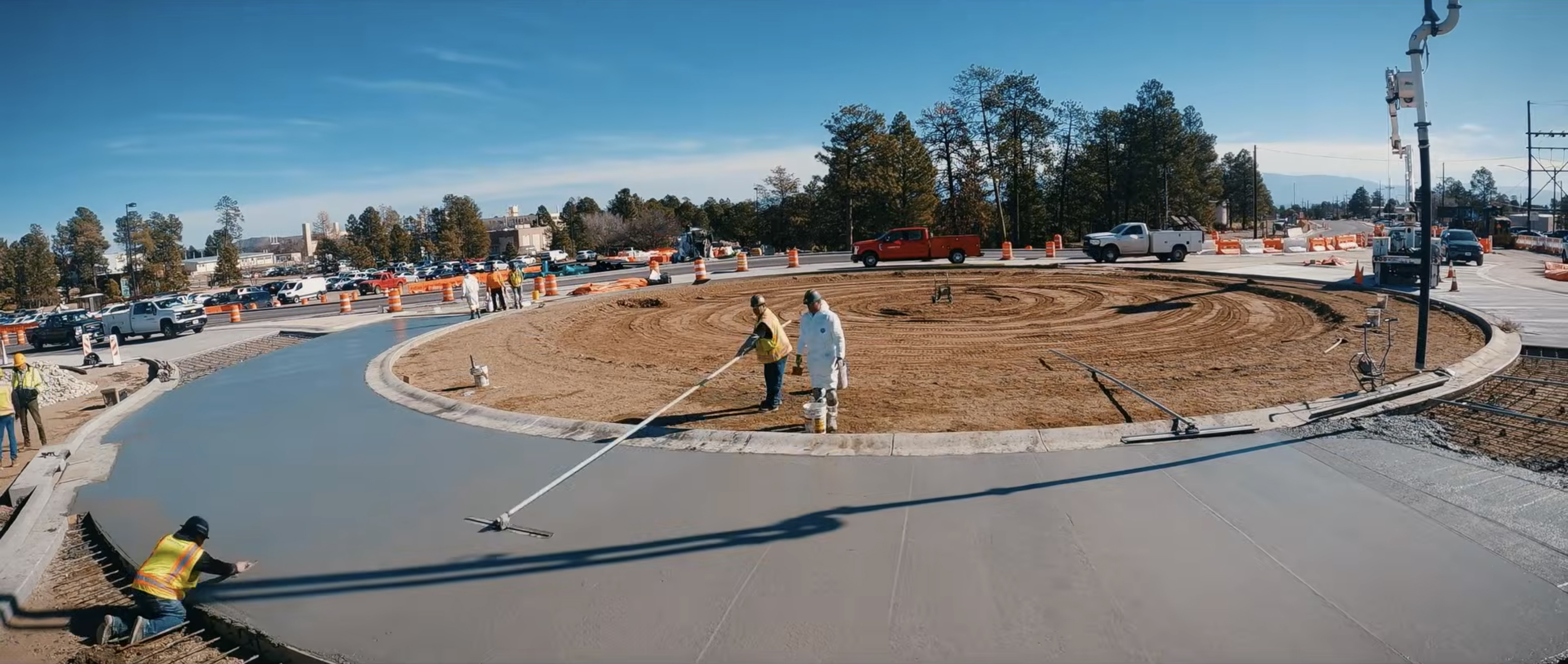 Construction workers smooth freshly poured concrete around a roundabout.