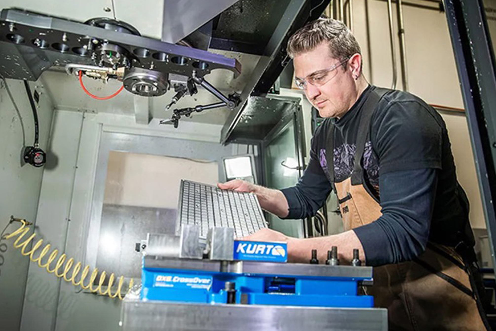 Machinist Jesse Hesch wears safety glasses as he positions a metal workpiece in a milling machine.